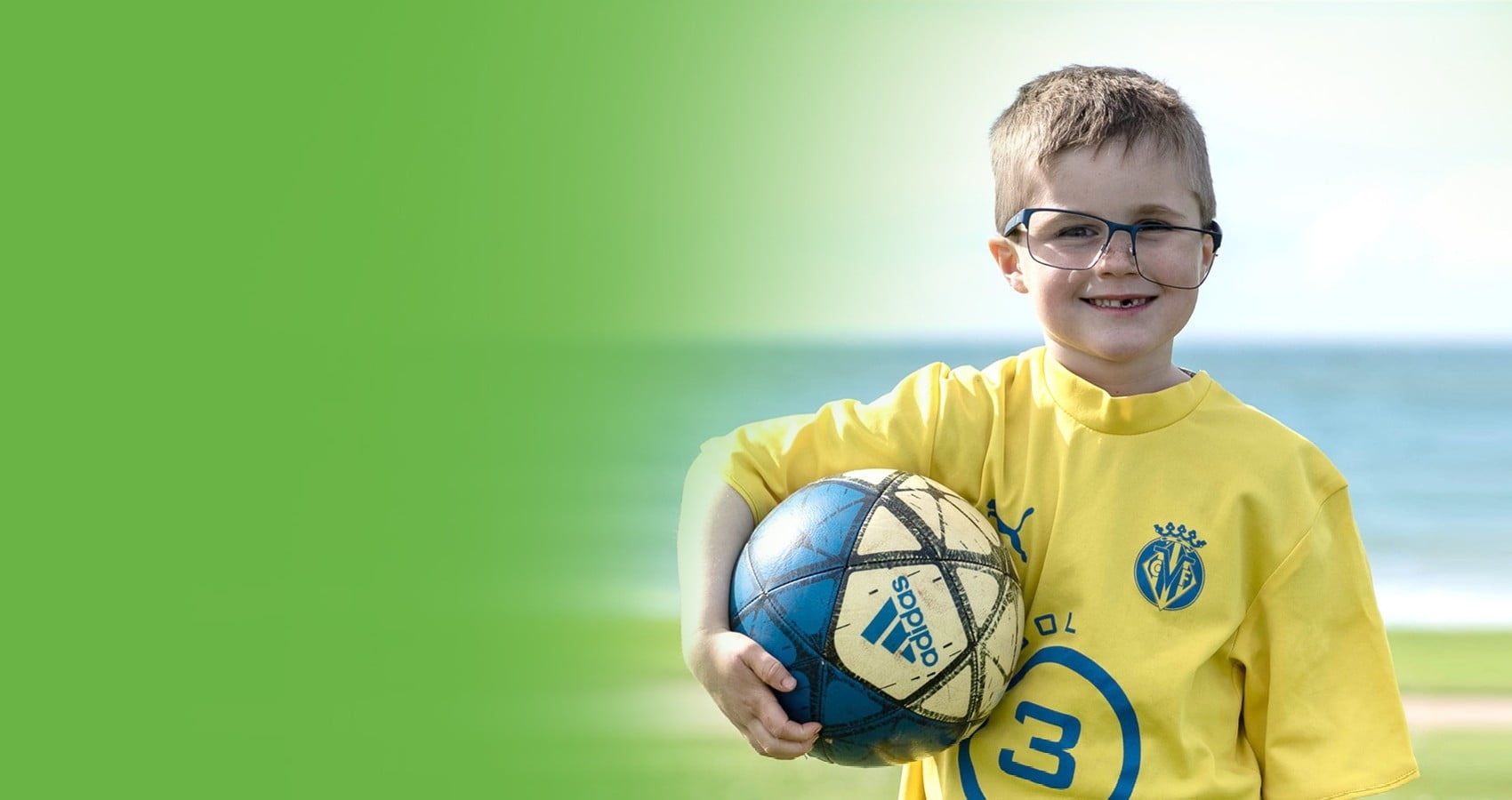 Smiling boy in glasses holding a soccer ball in front of water » HCi