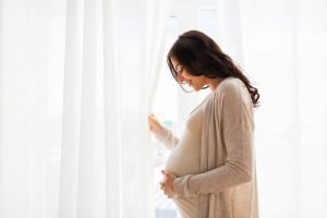 pregnant-woman-window-shutterstock_431039377-1 » HCi Pregnant woman standing by a window and holding her belly, smiling and enjoying good health with her pregnancy cover » HCi