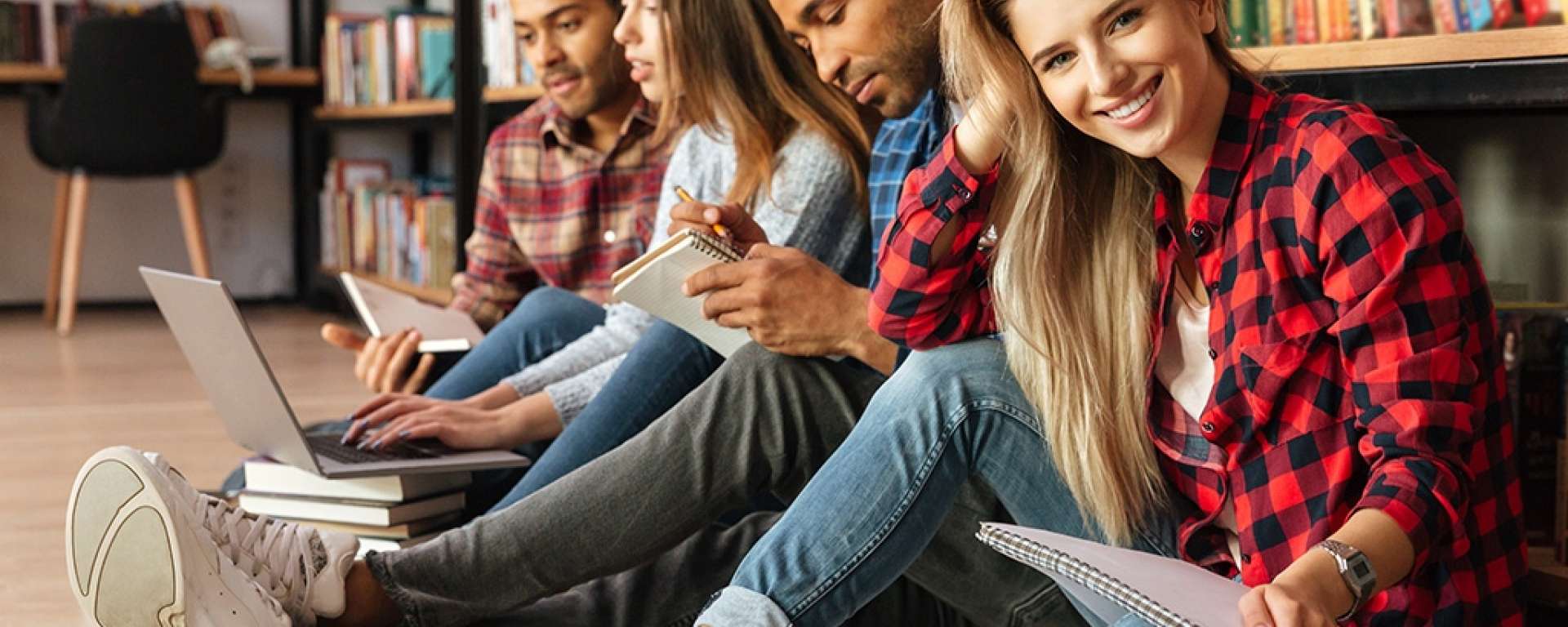 row of healthy young people sitting on the floor with notepads in a library