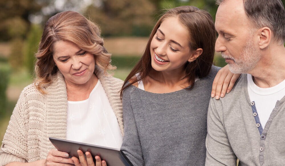 Mature couple and adult daughter looking at a tablet and smiling in the outdoors