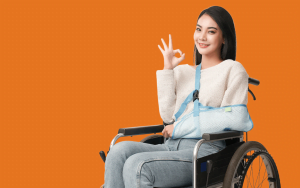 girl_wheelchair_sling_orange_background_shutterstock_1986977663-125kb » HCi Young woman sitting in a wheelchair, arm in a sling, smiling and making an okay sign after her ambulance trip - grateful for accident cover and health insurance » HCi