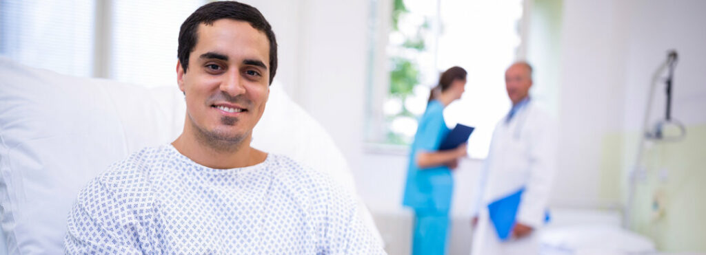 Man sitting in a hospital bed (inpatient) and smiling as a doctor and nurse talk in the background - HCi hospital contracts help members get quality care at value prices, reducing inpatient and outpatient costs