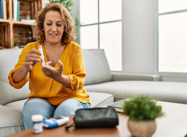 Woman in an orange top sitting on a couch and doing a diabetes finger prick to assess her blood sugar levels