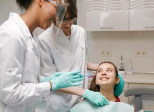A dentist and technician about to care for a girl's dental braces and teeth, thanks to HCi extras cover