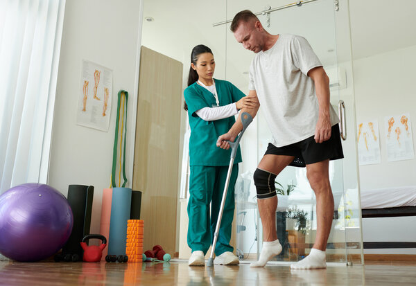 Physio helping a man in a knee support and using crutches in treatment and recovery. Claiming medical braces from HCi is easy.