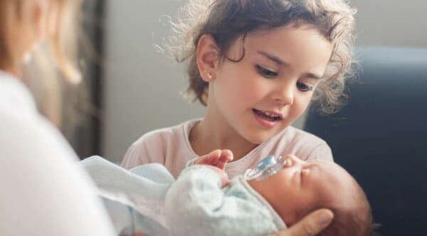 Little girl looking lovingly at a newborn baby - healthy baby, healthy relationships and health cover