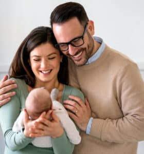 Smiling mother and father holding their newborn baby daughter at home » HCi Smiling mother and father holding their newborn baby. Adding a baby to HCi cover is easy » HCi