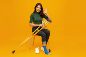woman-sitting-crutch-orange-background-shutterstock_1931763407-600x400 » HCi Woman sitting on a stool with injured foot and crutches, unable to work and needing financial help - on an orange background
