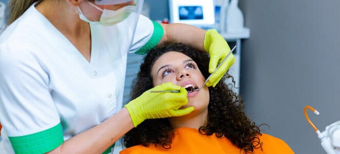 A female dentist working on teeth for a patient in an orange bib, covered by HCi extras cover