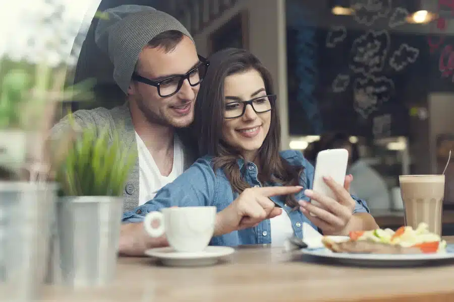 Smiling couple looking at a phone at a table, considering their private health insurance and limits for HCi extras cover